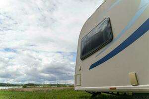 Camper trailer for traveling standing on shore of the lake in summer photo