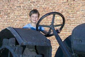 a boy driving an old vintage tractor in the background of a brick wall photo