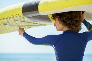 Happy woman in curly hair lifting yellow SUP board photo