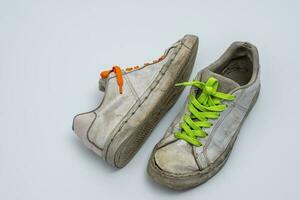 worn old torn white sneakers with colored laces on a white background photo