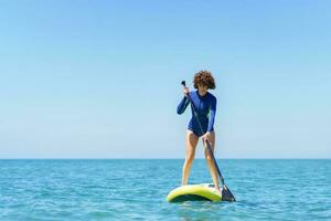 Rizado pelo mujer con paddleboard en mar foto