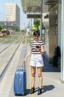 Positive woman with suitcase browsing smartphone on street photo