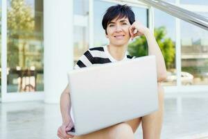 Joyful adult woman with laptop looking at camera on street photo