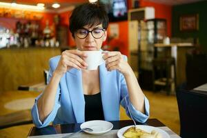 Calm middle aged woman enjoying hot coffee in cafe photo