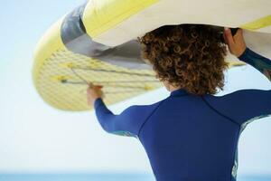 Unrecognizable woman lifting paddleboard over head on shore photo