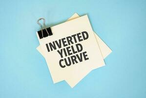 Text INVERTED YIELD CURVE on sticky notes with copy space and paper clip isolated on red background.Finance and economics concept. photo