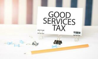 GOOD SERVICES TAX sign on paper on white desk with office tools. Blue and white background photo