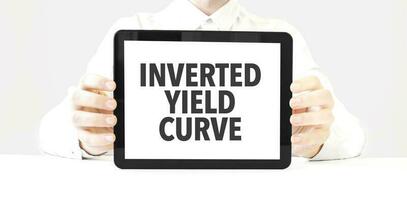 Text INVERTED YIELD CURVE on tablet display in businessman hands on the white background. Business concept photo