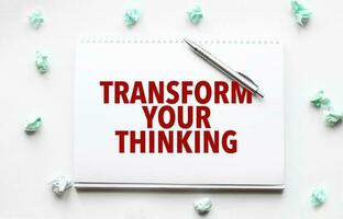 Blank sheet, pen and crumpled paper balls on grey table, flat lay. Text TRANSFORM YOUR THINKING photo
