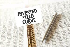 Text INVERTED YIELD CURVE on paper card, pen, financial documentation on table photo