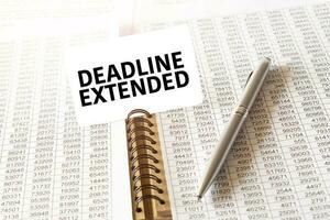 Text DEADLINE EXTENDED on paper card, pen, financial documentation on table photo