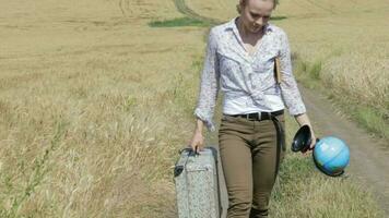 Young lady wearing jeans with luggage walking in the middle of the wheat field video