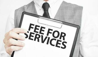 fee for services inscription on a notebook in the hands of a businessman on a grey background, a man points with a finger to the text photo