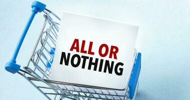 Shopping cart and text ALL OR NOTHING on white paper note list. Shopping list concept on blue background. photo