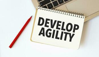 Laptop, red pen and notepad with text DEVELOP AGILITY in the white background photo