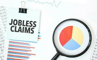 Green card on the white notepad and magnifier on the financial documentation. Text JOBLESS CLAIMS. Business concept photo