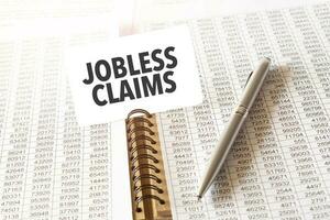 Text JOBLESS CLAIMS on paper card, pen, financial documentation on table photo