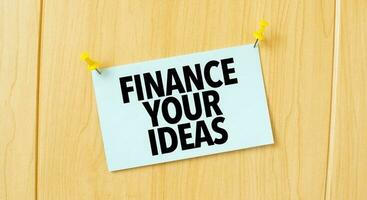 FINANCE YOUR IDEAS sign written on sticky note pinned on wooden wall photo