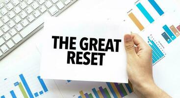 Businessman holding a card with text THE GREAT RESET .Keyboard, diagram and white background photo