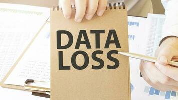 Text DATA LOSS on brown paper notepad in businessman hands on the table with diagram. Business concept photo