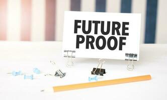 FUTURE PROOF sign on paper on white desk with office tools. Blue and white background photo