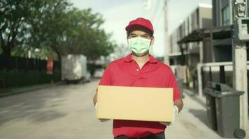 un' pacco consegna lavoratore indossare un' rosso uniforme indossa un' protettivo maschera. passaggio al di sopra di il pacchetto per il destinatario di il telecamera Visualizza anziché di il del ricevitore nel davanti di il Casa video