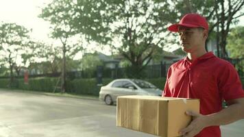 een pakket levering arbeider vervelend een rood uniform is Holding een pakket doos naar de ontvanger. contact de ontvanger in voorkant van de huis video