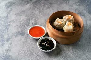 Chinese steamed dumplings or  Dim Sum with chopstick in bamboo steamer on dark abstract background photo