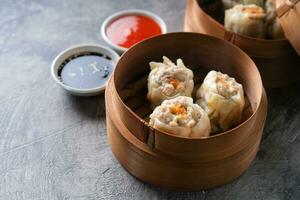 Chinese steamed dumplings or  Dim Sum with chopstick in bamboo steamer on dark abstract background photo