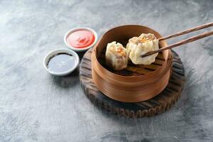 Chinese steamed dumplings or  Dim Sum with chopstick in bamboo steamer on dark abstract background photo