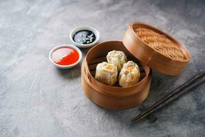 Chinese steamed dumplings or  Dim Sum with chopstick in bamboo steamer on dark abstract background photo