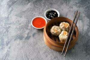 Chinese steamed dumplings or  Dim Sum with chopstick in bamboo steamer on dark abstract background photo