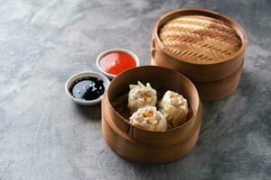 Chinese steamed dumplings or  Dim Sum with chopstick in bamboo steamer on dark abstract background photo