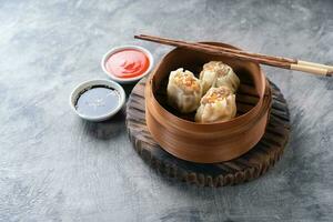 Chinese steamed dumplings or  Dim Sum with chopstick in bamboo steamer on dark abstract background photo