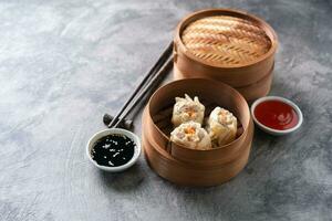 Chinese steamed dumplings or  Dim Sum with chopstick in bamboo steamer on dark abstract background photo