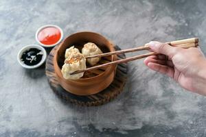 Chinese steamed dumplings or  Dim Sum with chopstick in bamboo steamer on dark abstract background photo