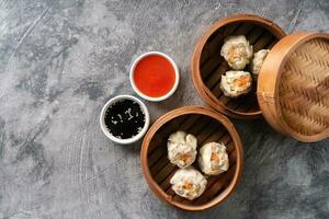 Chinese steamed dumplings or  Dim Sum with chopstick in bamboo steamer on dark abstract background photo