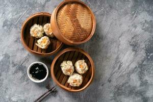 Chinese steamed dumplings or  Dim Sum with chopstick in bamboo steamer on dark abstract background photo