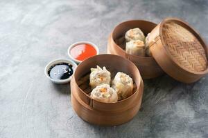 Chinese steamed dumplings or  Dim Sum with chopstick in bamboo steamer on dark abstract background photo