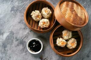 Chinese steamed dumplings or  Dim Sum with chopstick in bamboo steamer on dark abstract background photo