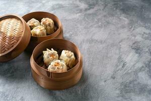 Chinese steamed dumplings or  Dim Sum with chopstick in bamboo steamer on dark abstract background photo