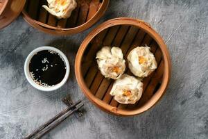 Chinese steamed dumplings or  Dim Sum with chopstick in bamboo steamer on dark abstract background photo