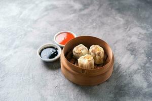 Chinese steamed dumplings or  Dim Sum with chopstick in bamboo steamer on dark abstract background photo