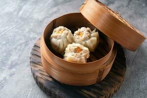 Chinese steamed dumplings or  Dim Sum with chopstick in bamboo steamer on dark abstract background photo