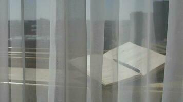 Diary with a pen at marble sill of an open window. Blowing grey transparent curtains video