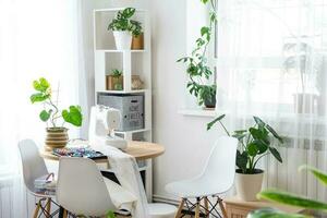 Sewing machine on a round table in the white interior of the house near the window with a transparent curtain, and a home plant in a pot - a modern interior. hobby, home business photo