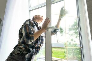 mujer a mano lavados el ventana de el casa con un trapo con rociar limpiador y fregona dentro el interior con blanco cortinas restaurar orden y limpieza en el primavera, limpieza servise foto