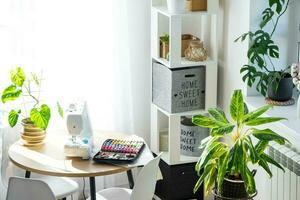 Sewing machine on a round table in the white interior of the house near the window with a transparent curtain, and a home plant in a pot - a modern interior. hobby, home business photo