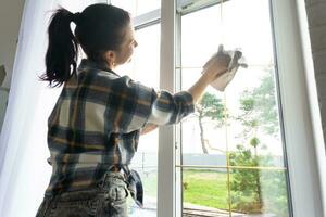 Woman manually washes the window of the house with a rag with spray cleaner and mop inside the interior with white curtains. Restoring order and cleanliness in the spring, cleaning servise photo