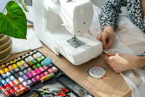 Woman hand close up sews tulle on electric sewing machine. Filling the thread into the sewing needle, adjusting the tension. Comfort in the house, a housewife's hobby, layout of sewing tools photo